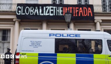 A police van is parked outside the Diorama building in London with a police officer standing next to it, and above the van is a banner reading 'Globalize the intifada' hung on the building, in 2023.