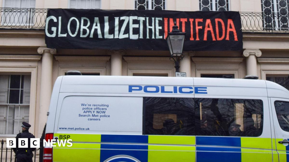 A police van is parked outside the Diorama building in London with a police officer standing next to it, and above the van is a banner reading 'Globalize the intifada' hung on the building, in 2023.