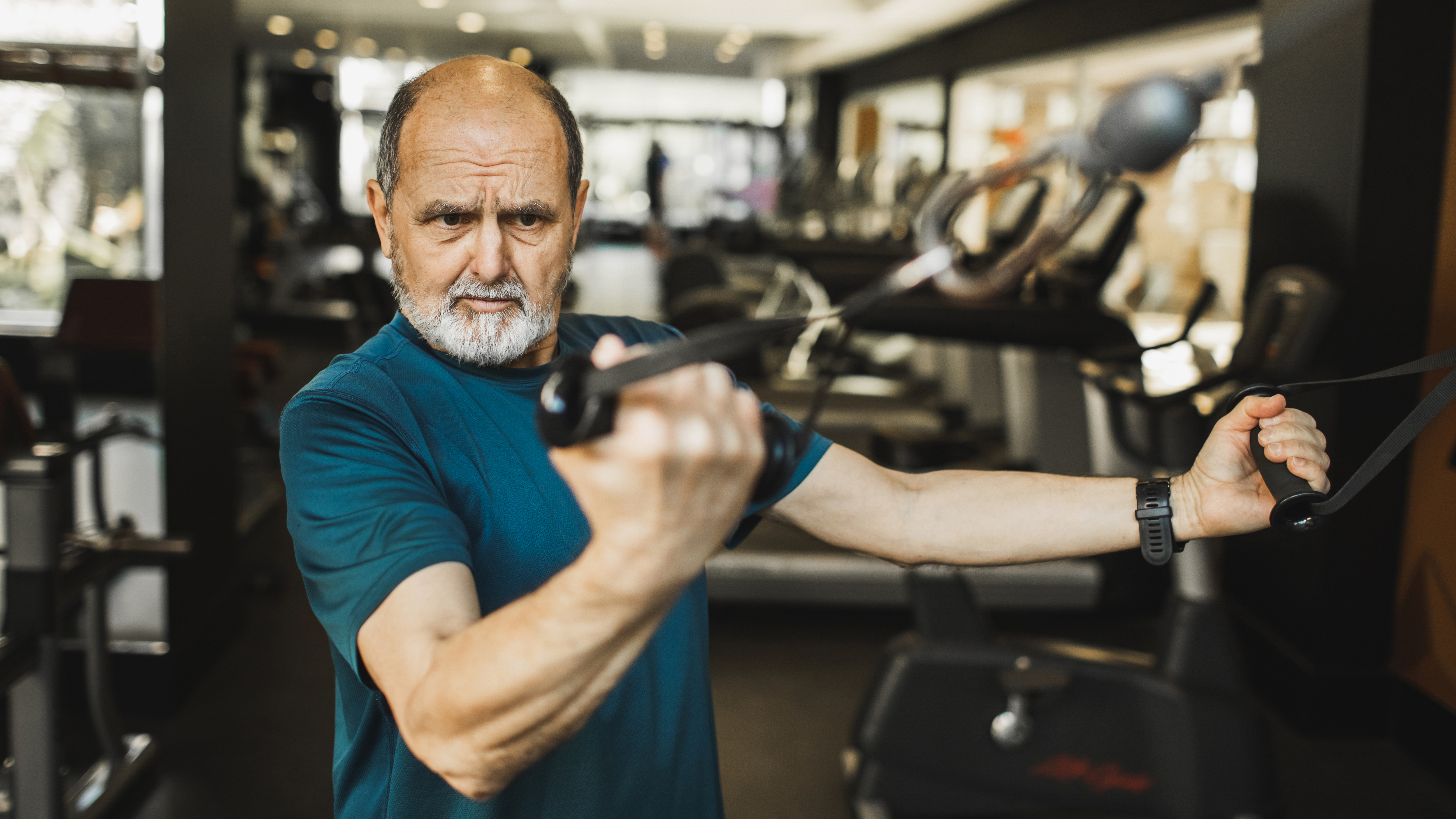 A man in a gym is exercising on a cable machine, holding two handles in his hands and concentrating on his grip.