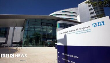 An exterior view of the Queen Elizabeth hospital showing a large building with glass frontage leading to its reception area