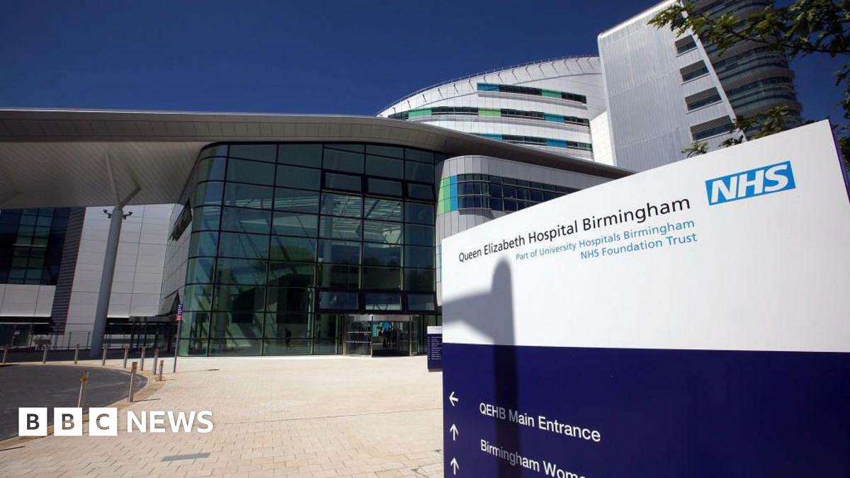 An exterior view of the Queen Elizabeth hospital showing a large building with glass frontage leading to its reception area