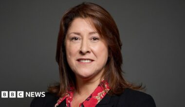 Michelle Scrogham has long brown hair and is wearing a black jacket. She is posing for an official portrait.