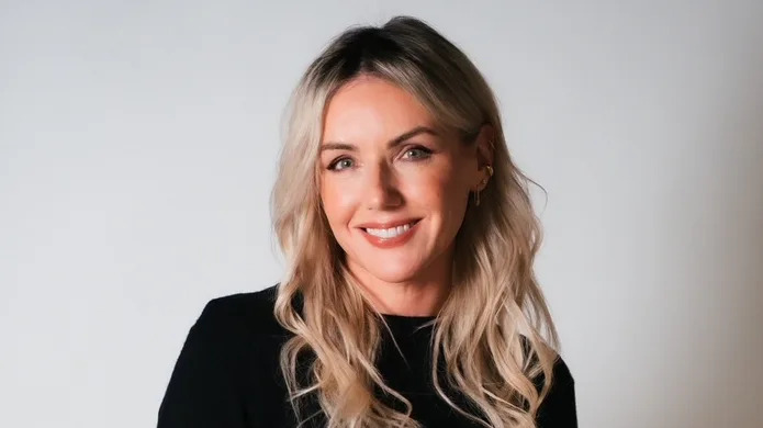 Sali wears a black top and is smiling at the camera. It's a professional headshot.  She has long wavy blonde hair. 