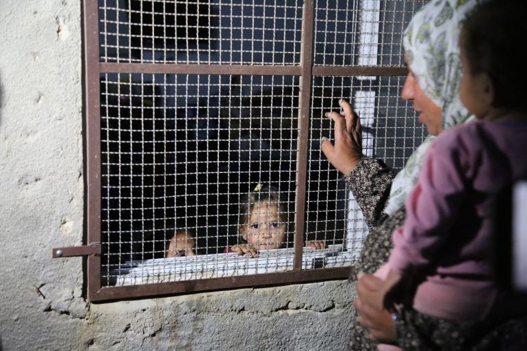 Hamida Hamamda in her yard with her grandchilren. One of her granddaughters stands in the house, behind the metal grates they had to install to try to protect themselves froms settlers