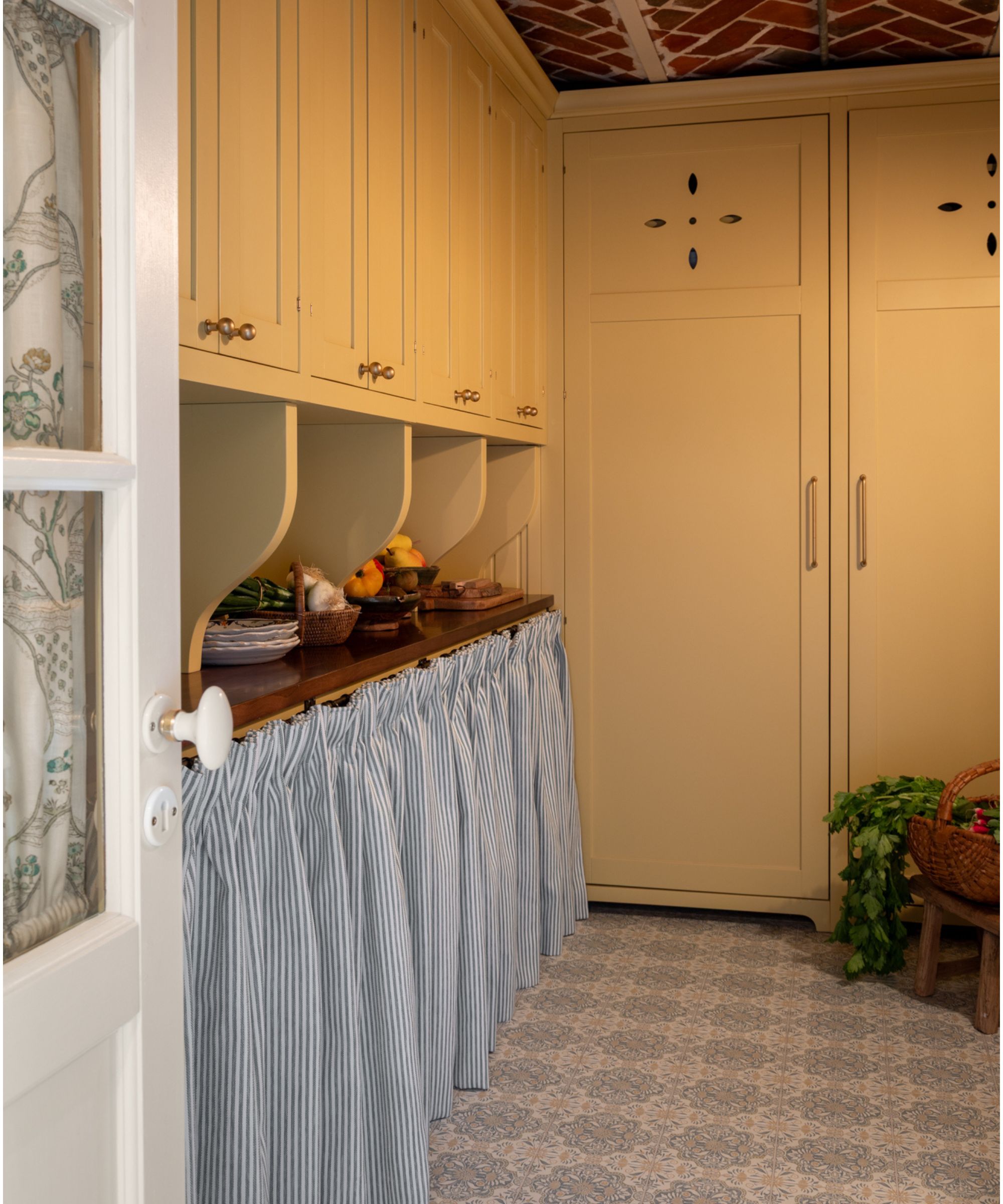 rustic vintage style pantry with ochre yellow cabinetry, tiled floor, a blue and white striped cabinet skirt