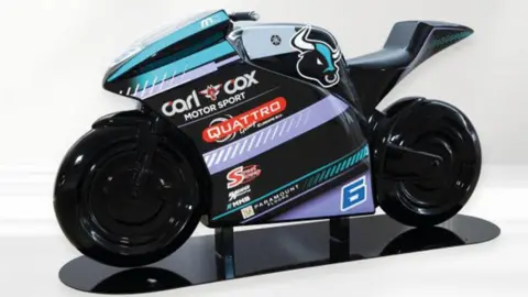 IOM TT The model of Michael Dunlop's bike, which is black, turquoise and purple and has Carl Cox's team logo on the side. It it on a black stand against a white background.