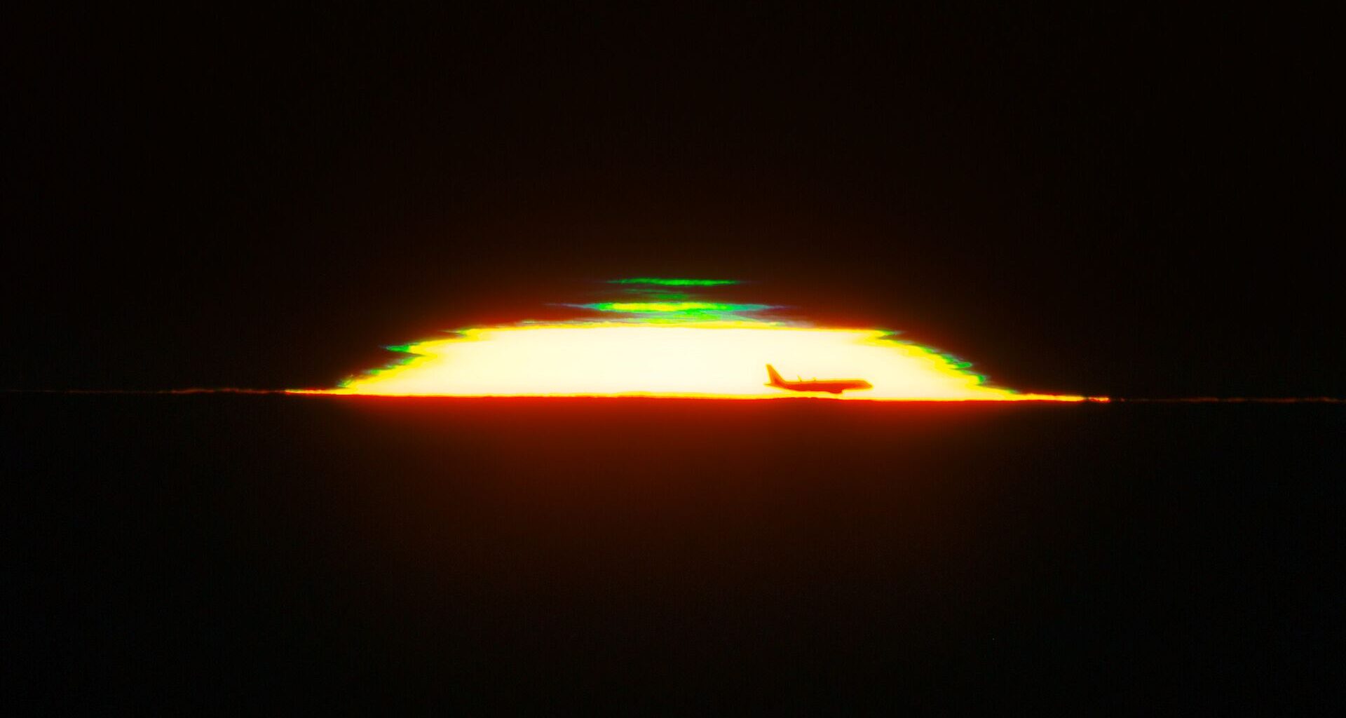 The half dome of a glowing sunset is seen against a black sky with the silhouette of an airplane in the front and a green shape above it.