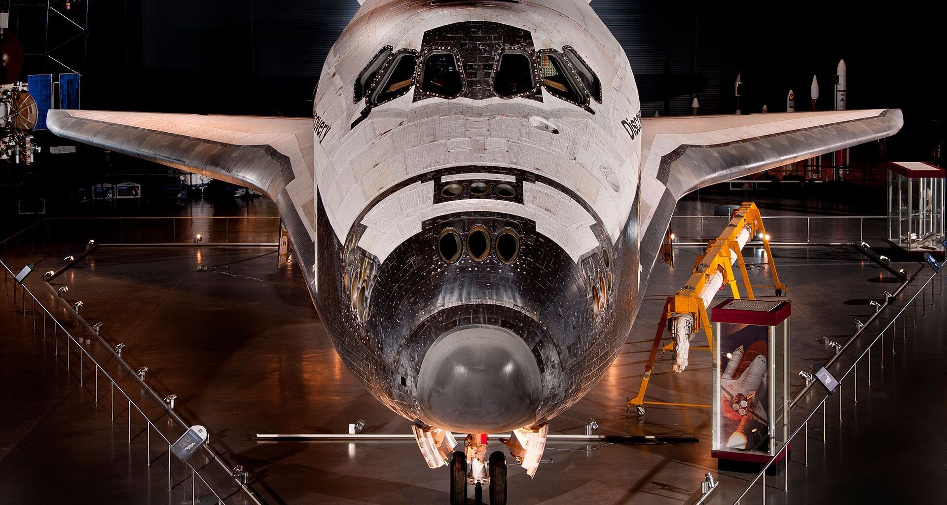a winged back and white orbiter standing on its landing gear is seen on museum display
