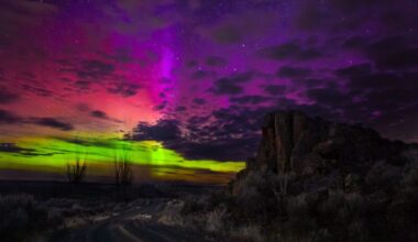 Forms of aurora: Rainbow colors of light near the horizon with dark clouds blocking patches and a dark rural landscape.