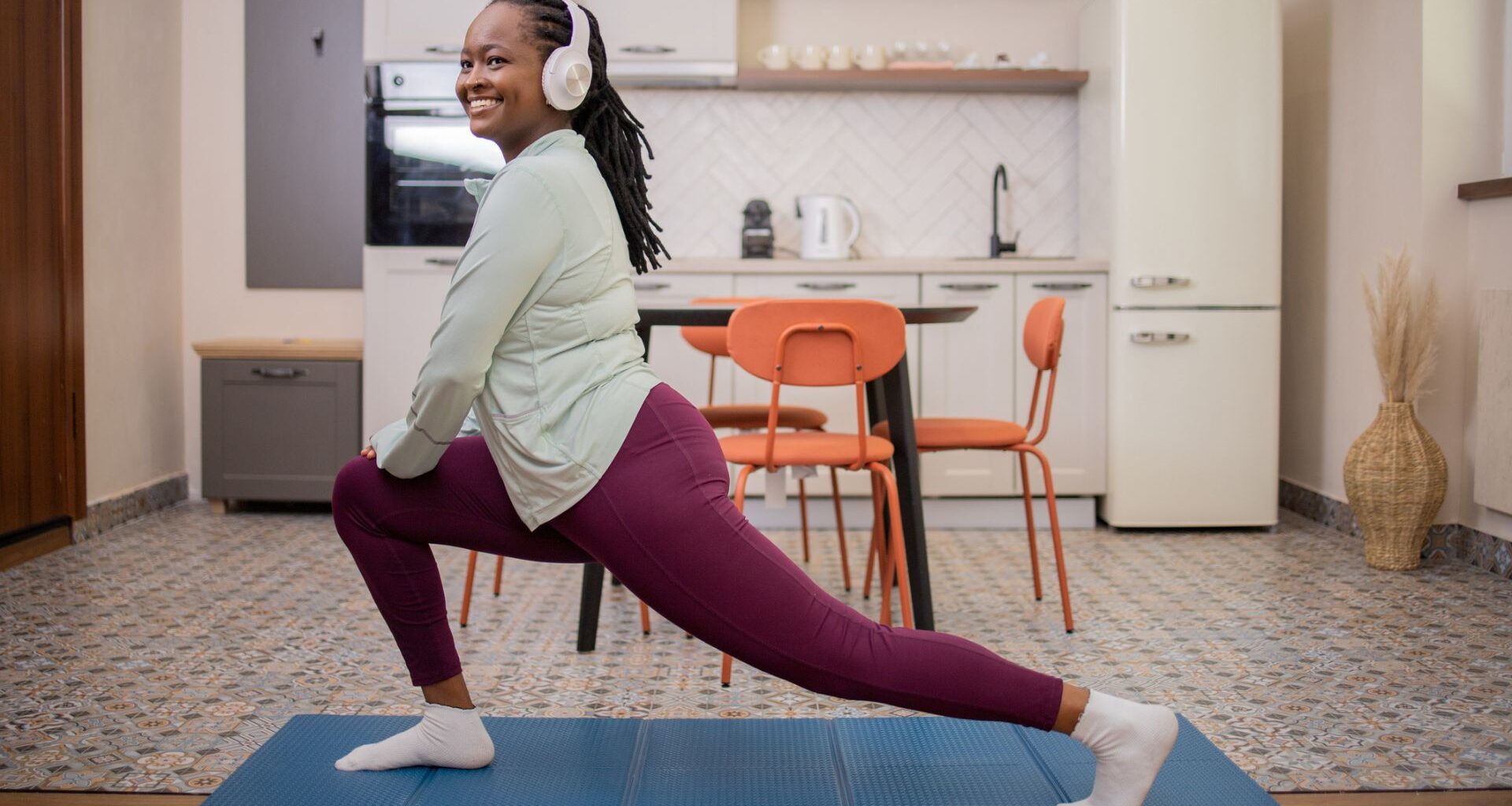 woman in headphones does a lunge stretch on a mat in her kitchen