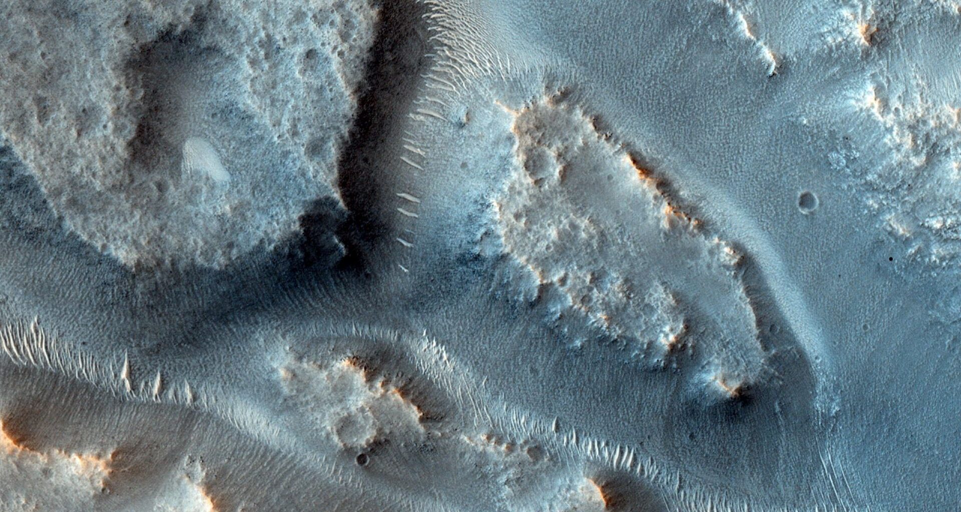 A close up of the surface of Mars showing blue dunes with streaks of ancient river basins between the dunes