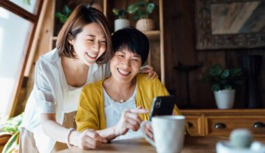 Affectionate Asian senior mother and daughter using smartphone together at home, smiling joyfully