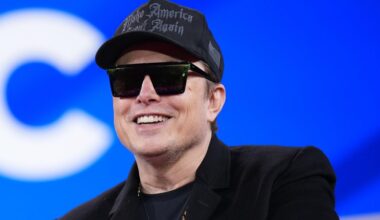 Satya Nadella clasps his hands together and speaks in front of a lilac background on stage.