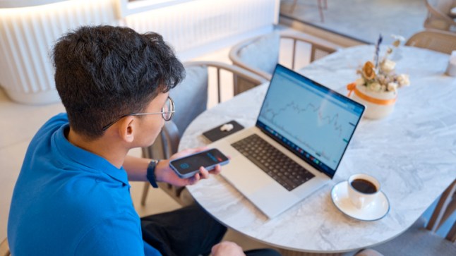 Young man analyzing stock market data using AI tools on laptop at a cafe