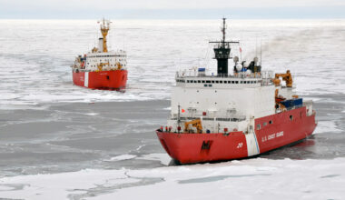Two large red and white ships cut through ice.