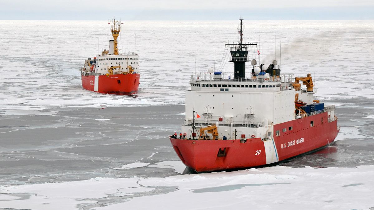 Two large red and white ships cut through ice.