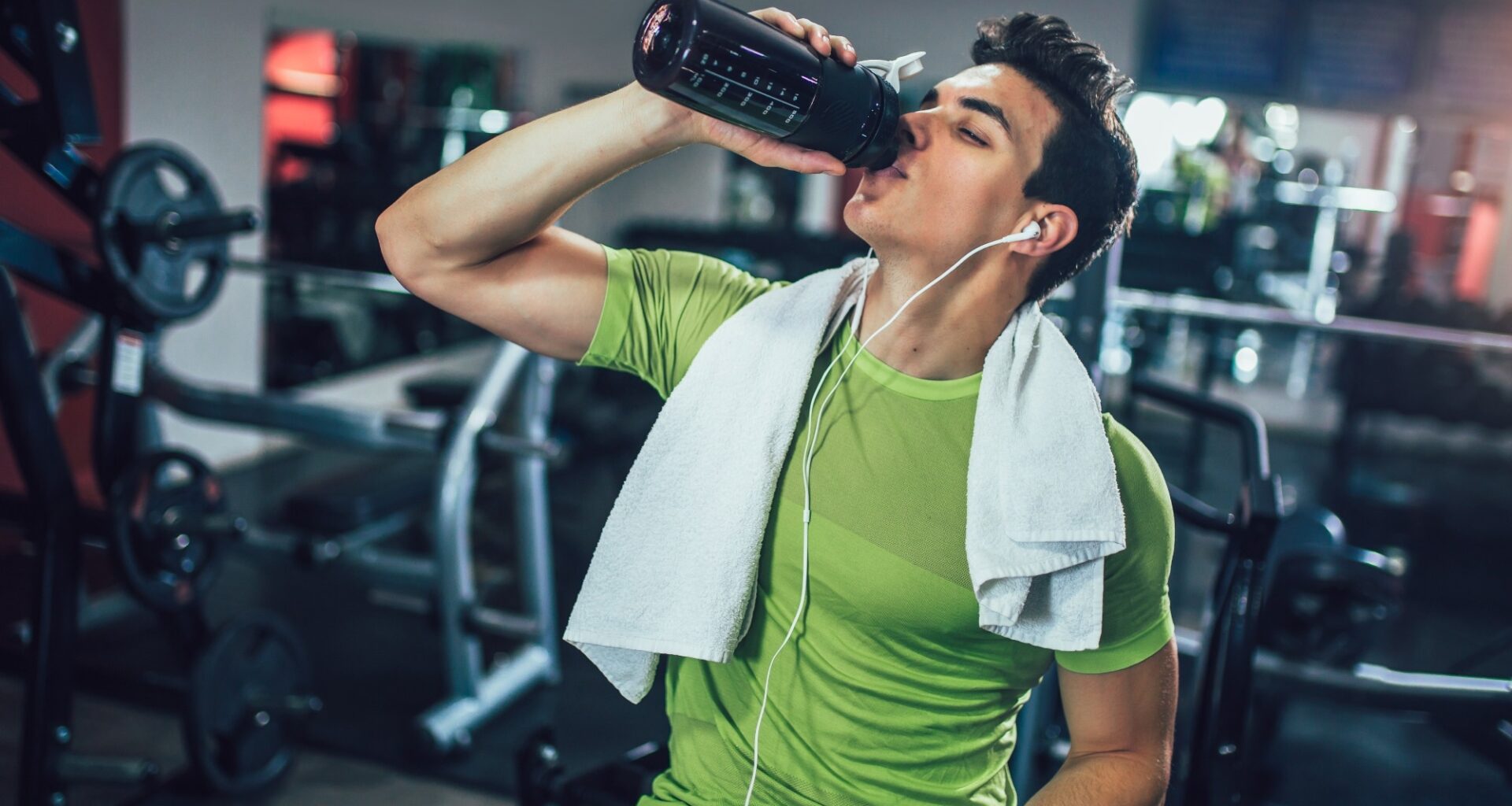 Young man drinking pre-workout drink from bottle in the gym