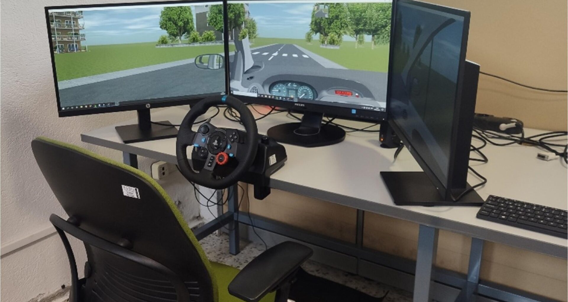 Driving simulator setup used in the experiments, consisting of a steering wheel with pedals, three monitors displaying the virtual driving environment, and a participant’s chair. Study: Cognitive alterations related to driving performance in Parkinson’s disease detected by a driving simulator 