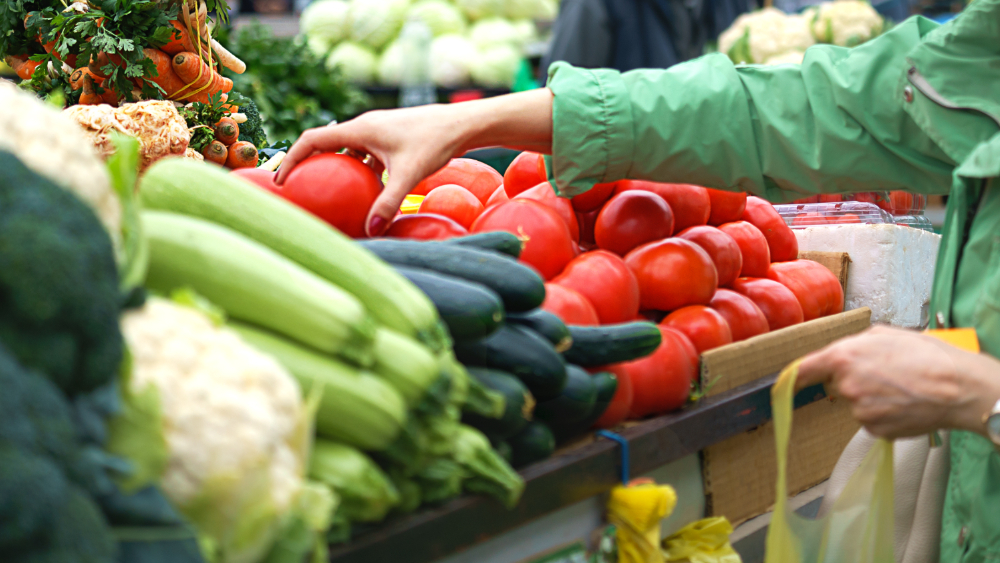 A person picking up fresh vegetables in an open market.