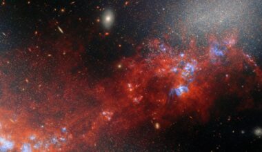 A glowing cloud of red gas and dust mixed in with bright dots for stars in deep space