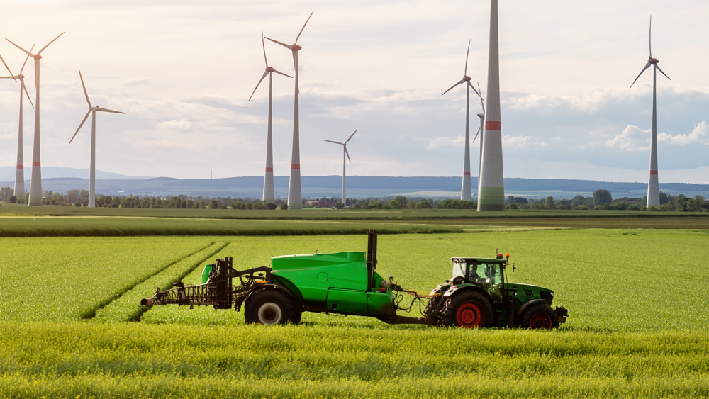 A tractor on a open field with windmills in the background.