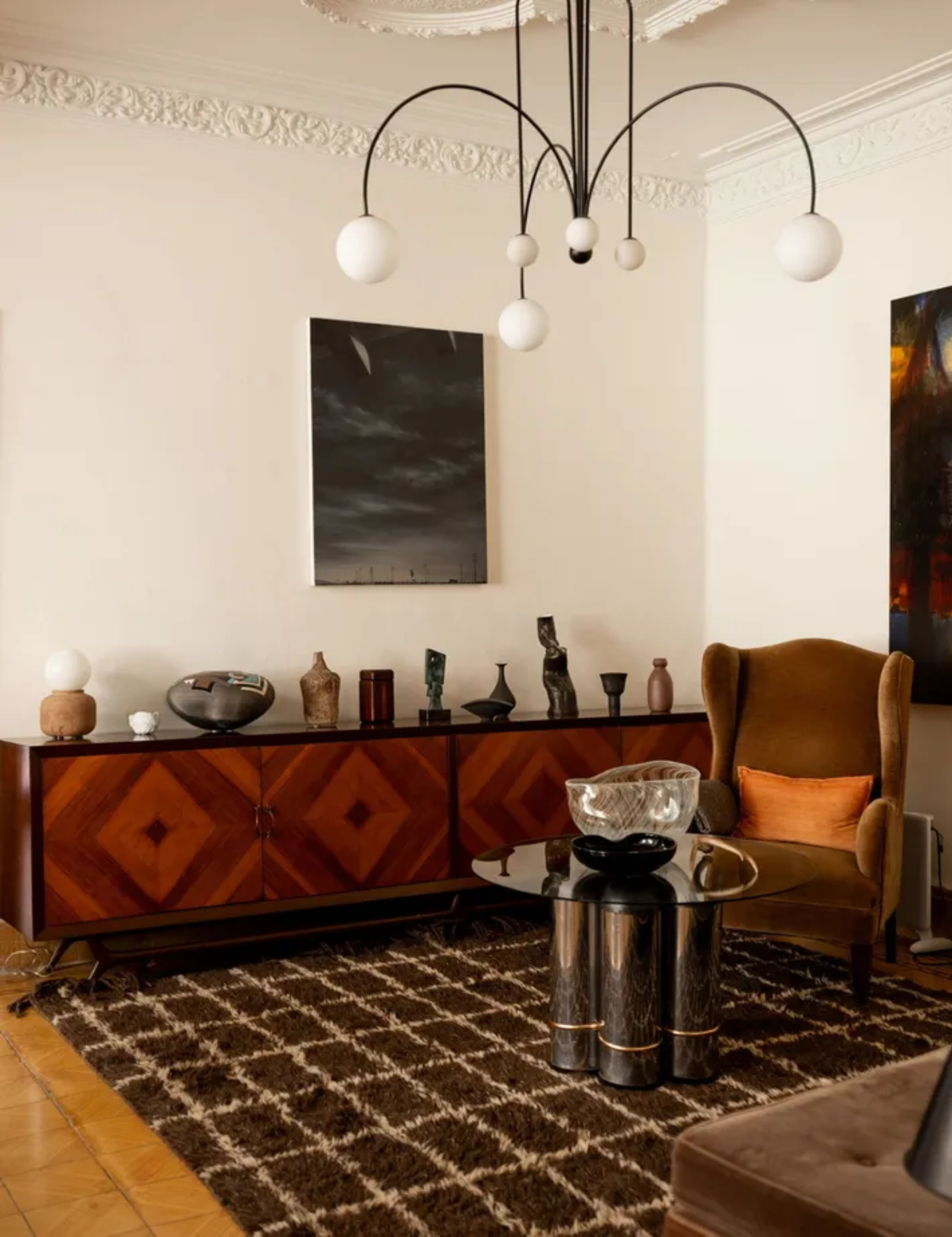 Contemporary living room with chequered rug, velvet armchair and wood cabinet holding a collection of ceramics and pottery