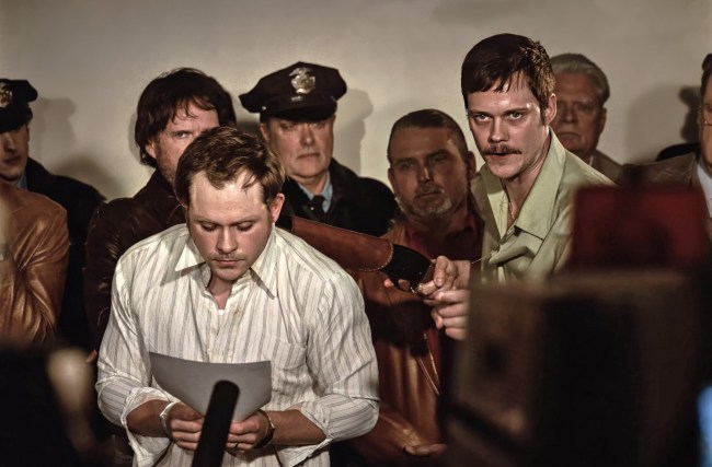 DEAD MAN'S WIRE, Dacre Montgomery (front, reading), Bill Skarsgard (right, mustache), 2025. © Row K Entertainment / Courtesy Everett Collection