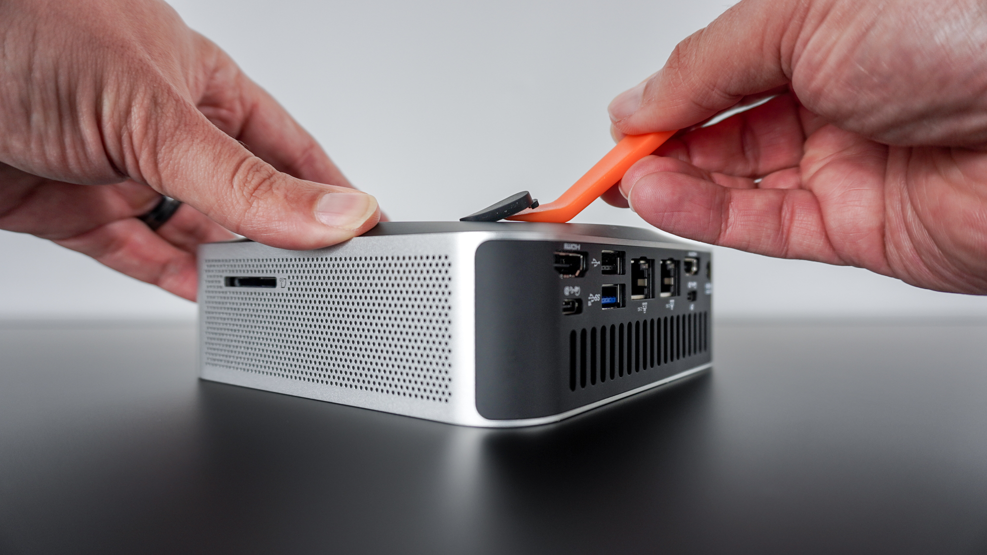 A person removing the rubber feet on the bottom of the Geekom A9 Max using a pry tool