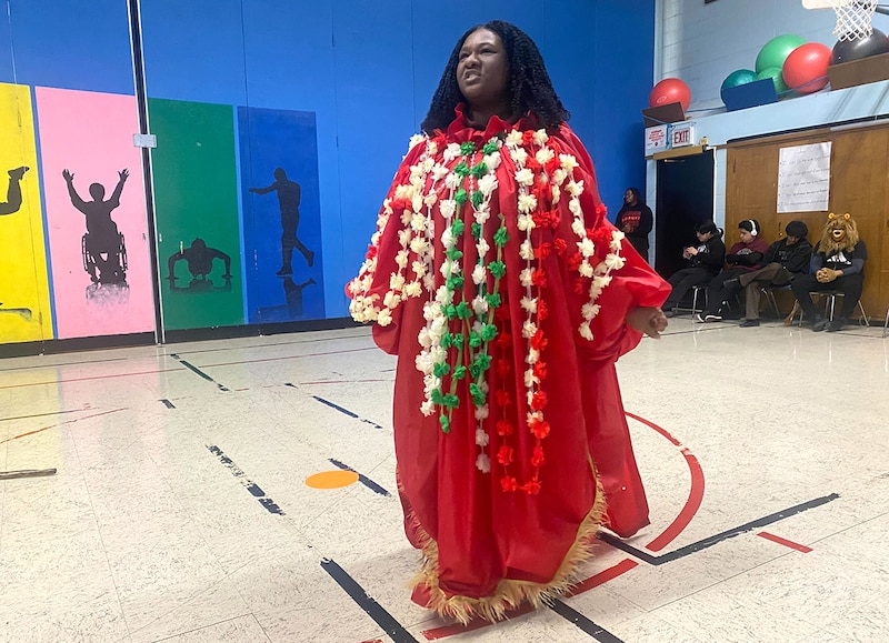 A student in a red costume performs in a gymnasium.