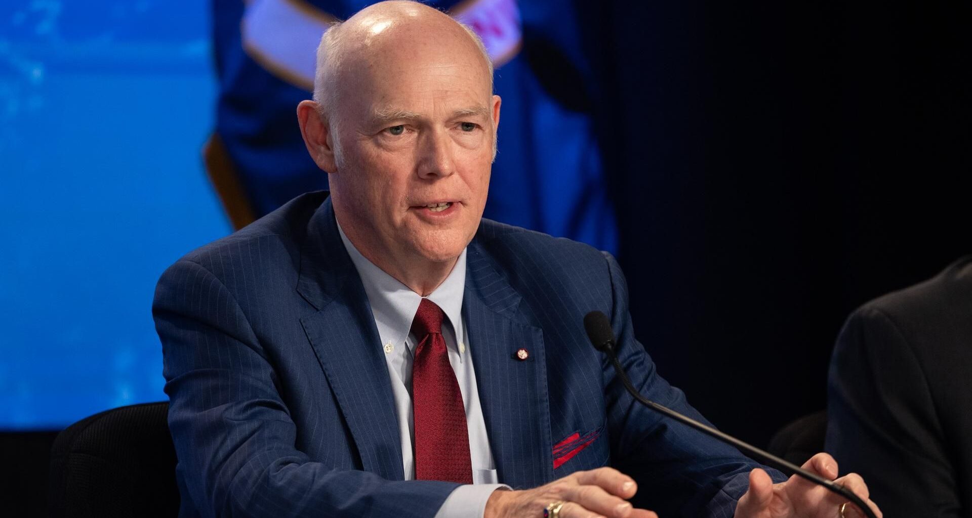 A man in a blue and white suit speaking into a microphone in a NASA press conference.