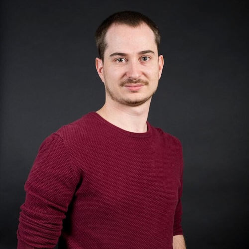 Smiling man with short hair wearing a brown shirt.