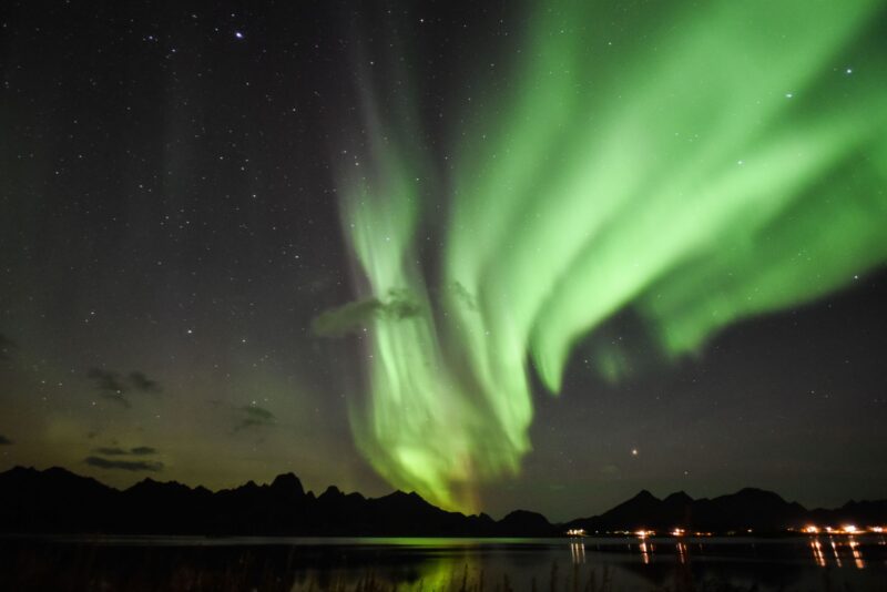 Green rows of aurora like layered drapes over a dark lake.