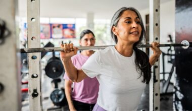 Woman lifting barbell in gym with support from friend from behind