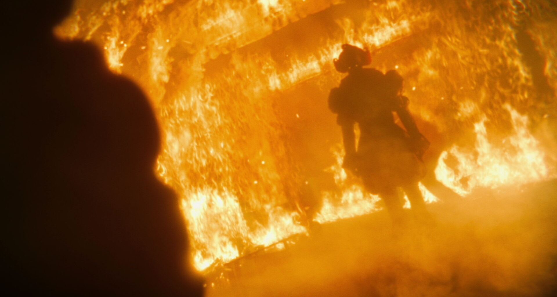 Bill Skarsgard as Pennywise standing in a burning building in It: Welcome to Derry