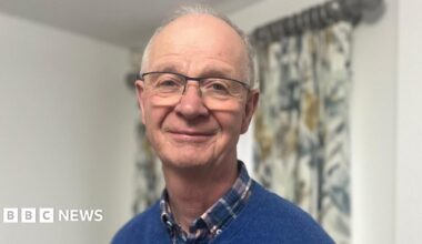 Alan Shepherd has short grey hair and metal glasses. He is wearing a checked shirt and blue sweatshirt.