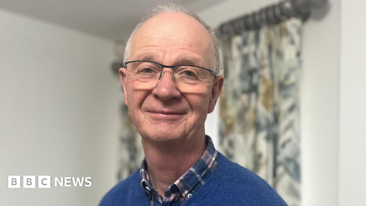 Alan Shepherd has short grey hair and metal glasses. He is wearing a checked shirt and blue sweatshirt.