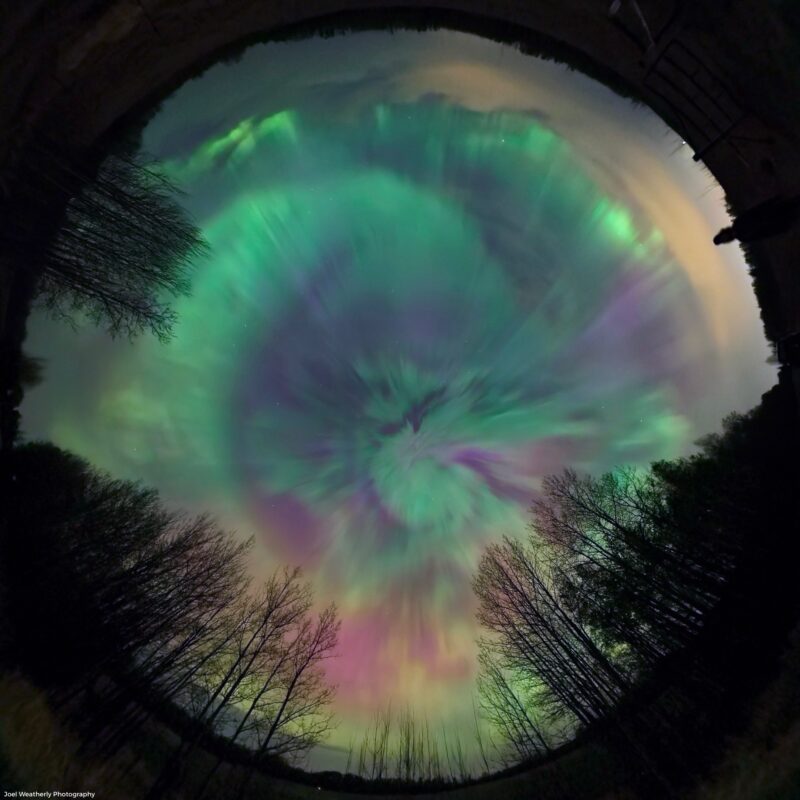 A fish-eye lens looking up at a 360 view of the sky with aurora everywhere including right overhead.