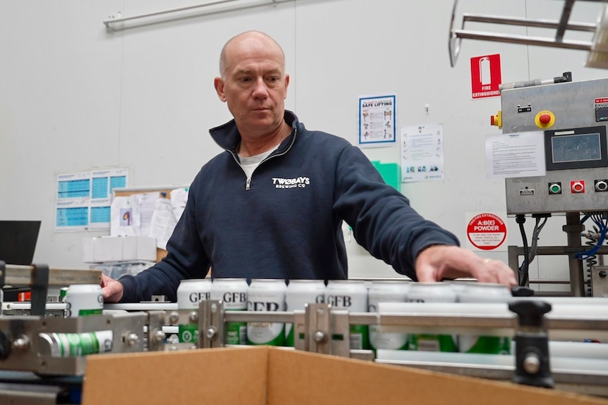 Richard Jeffares wears a blue jumper and checks beer cans on a production line.