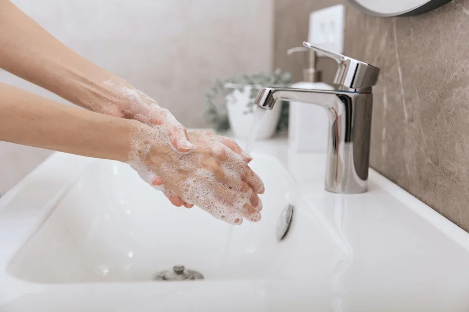 Hands being washed with soap in a bathroom sink, water running from a modern faucet