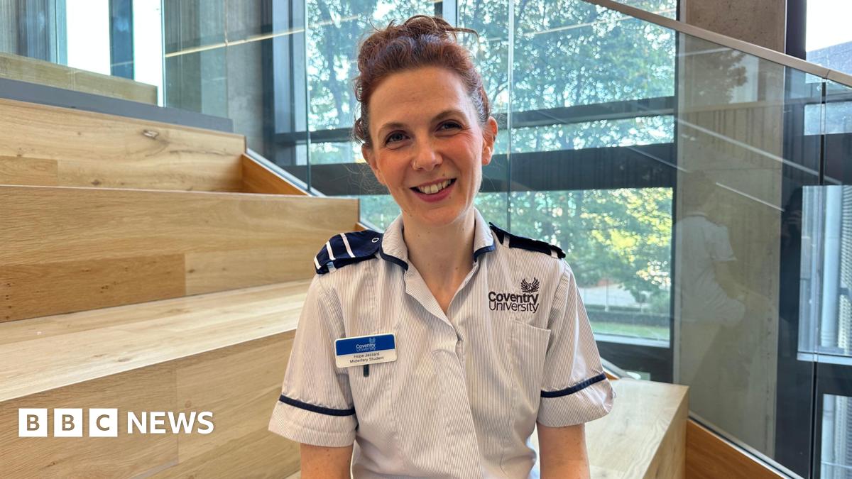 A woman with brown hair wearing a nurses uniform smiling.