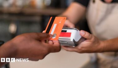 Contactless card payment being made with a card held in a hand and a terminal being held by someone in an apron.