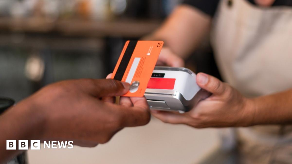 Contactless card payment being made with a card held in a hand and a terminal being held by someone in an apron.