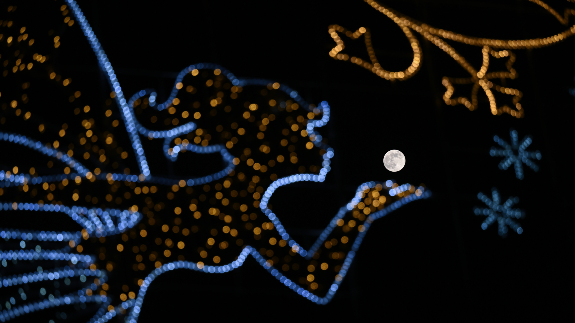 The full moon is pictured shining behind an LED light display in a black sky, which makes it appear as if the satellite is being gently held in the palm of a fairy made of artificial lights.