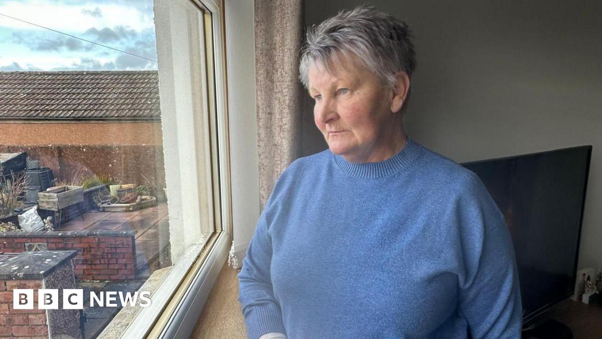 Nancy Dunnachie, who has short, grey hair, is wearing a blue knitted jumper and is staring out of a window