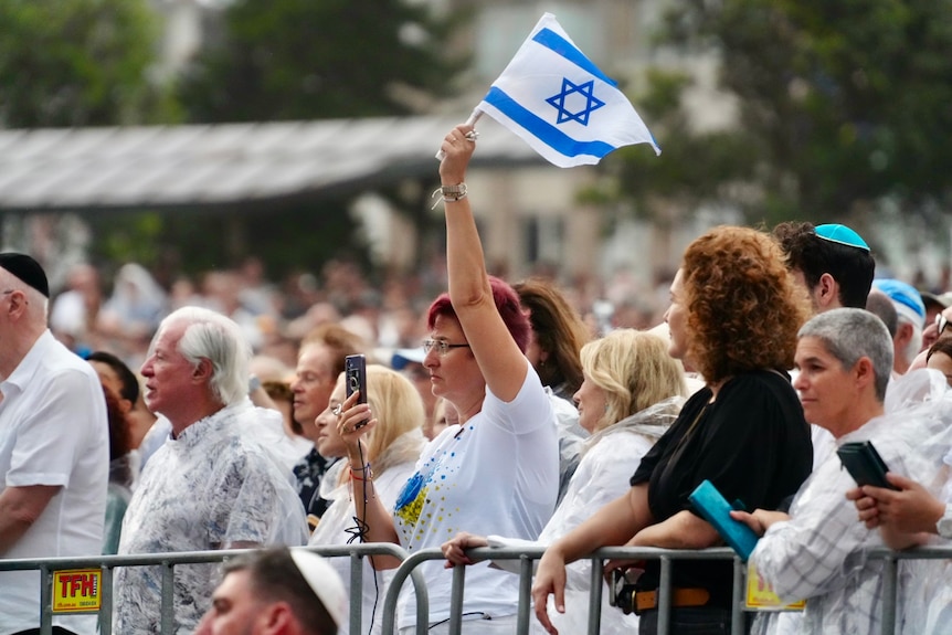 A woman at a memorial service holding up an Israeli flag.