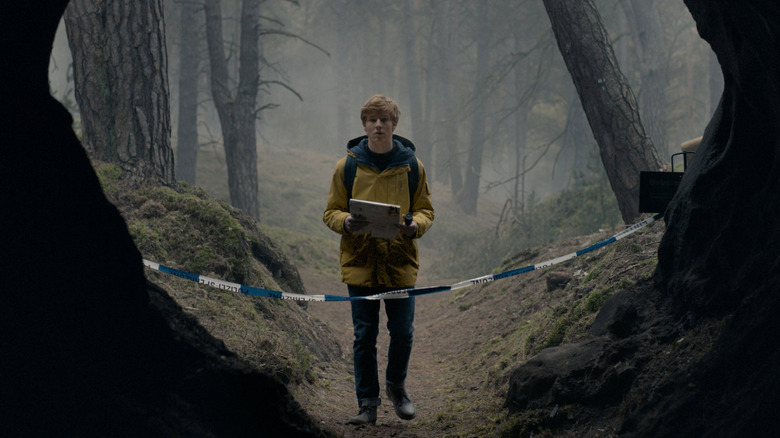 Jonas holding a notebook looking into a cave in Dark