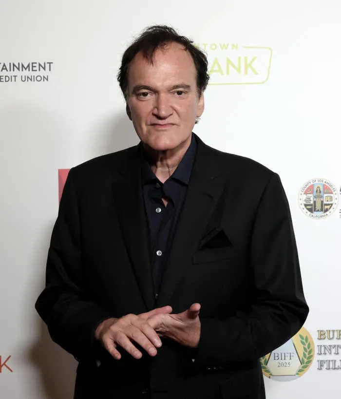 A person in a dark suit and black shirt poses on a red carpet at a film festival event
