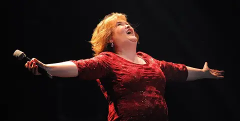 Andrew Yates/AFP via Getty Images Susan Boyle, wearing a red dress with her arms outstretched, sings during the musical "I Dreamed A Dream" at the Royal Theatre in Newcastle in 2012