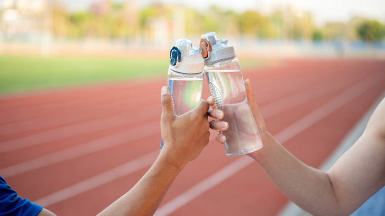 Two athletes holding and clinking their water bottles together on the racetrack.