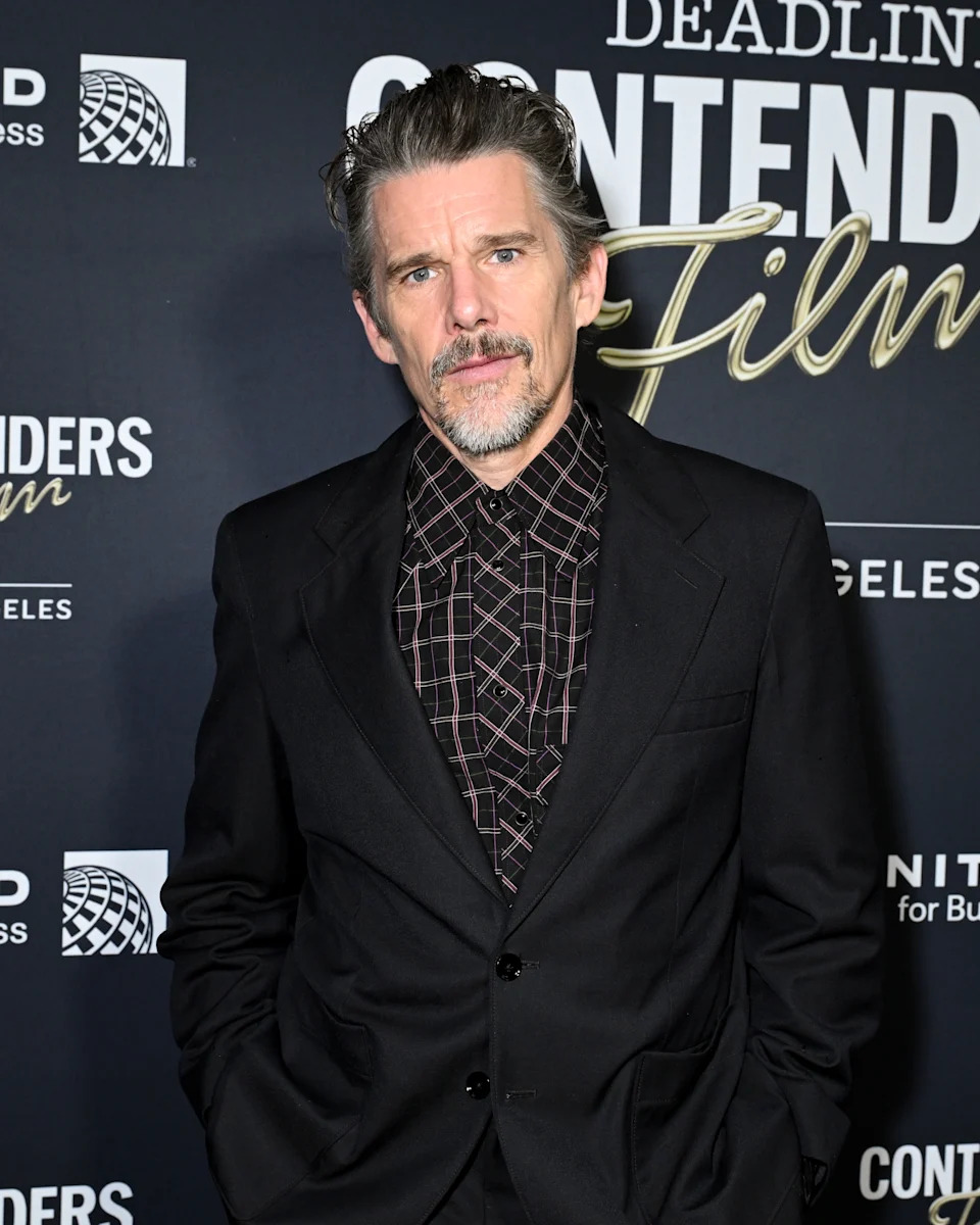 Actor in a patterned shirt and dark blazer poses on a red carpet at a Deadline event backdrop